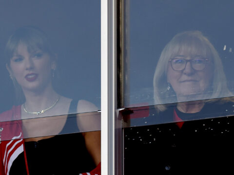 Taylor Swift and Donna Kelce look on before the game, peering through the glass of their box seats.