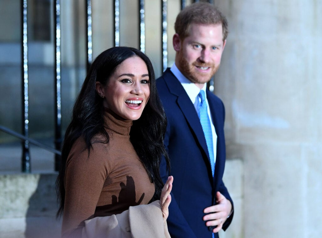 Prince Harry and Meghan Markle greet supporters and press outdoors.