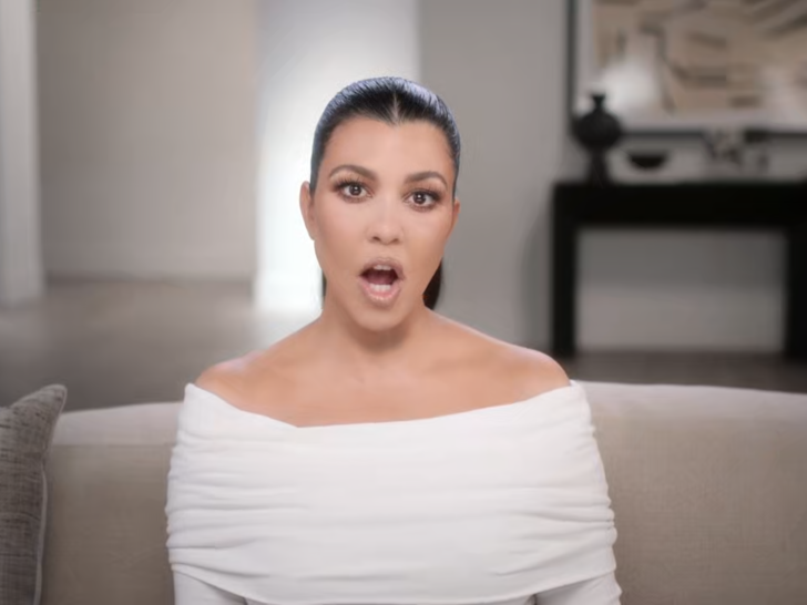 Kourtney Kardashian tells the confessional camera what she's thinking with her mouth open, wearing a wide-necked white blouse.
