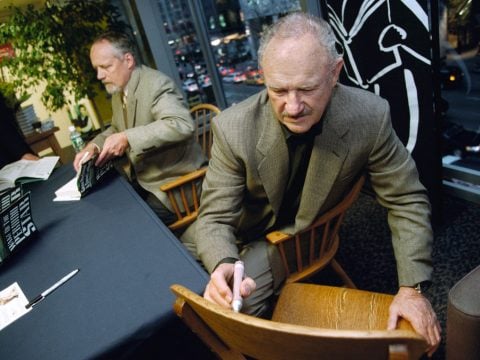 Gene Hackman signs a chair for a fan while also signing posters from his movie 