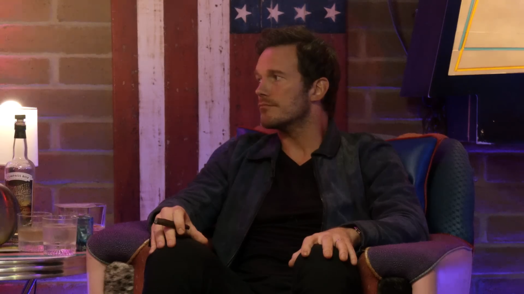 Chris Pratt holds a cigar while seated.