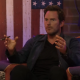 Chris Pratt gestures while holding a cigar and in front of a painted American flag.