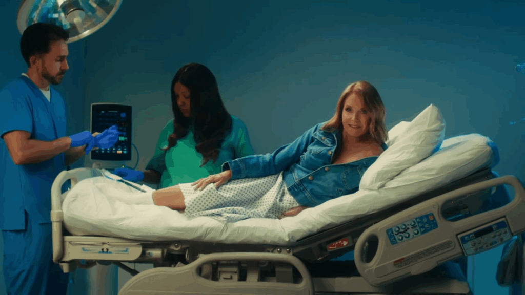 Katie Couric in a PSA while wearing a jean jacket and a hospital gown.