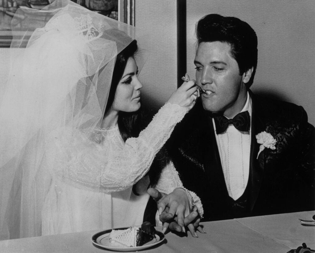 Elvis Presley (1935 - 1977) being fed a mouthful of wedding cake by his bride Priscilla Beaulieu at the Aladdin Hotel, Las Vegas.   