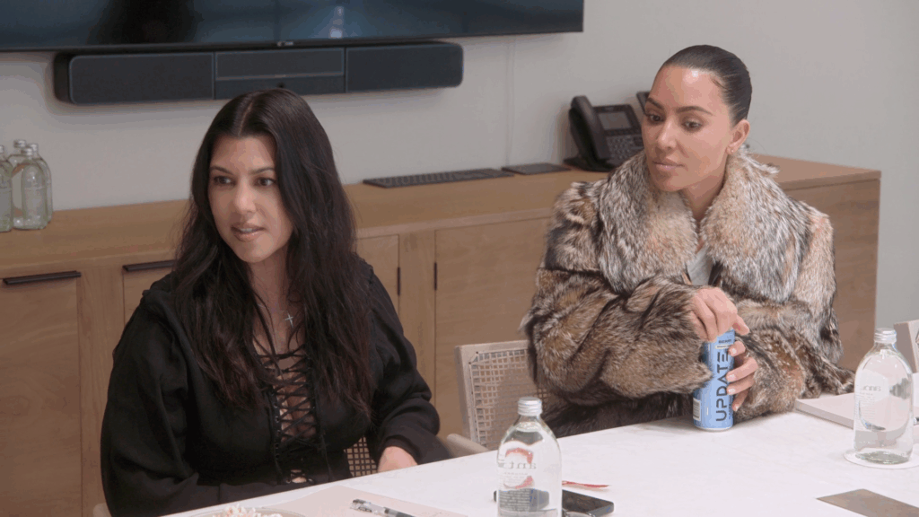 Kourtney Kardashian and Kim Kardashian on 'The Kardashians' at a table.