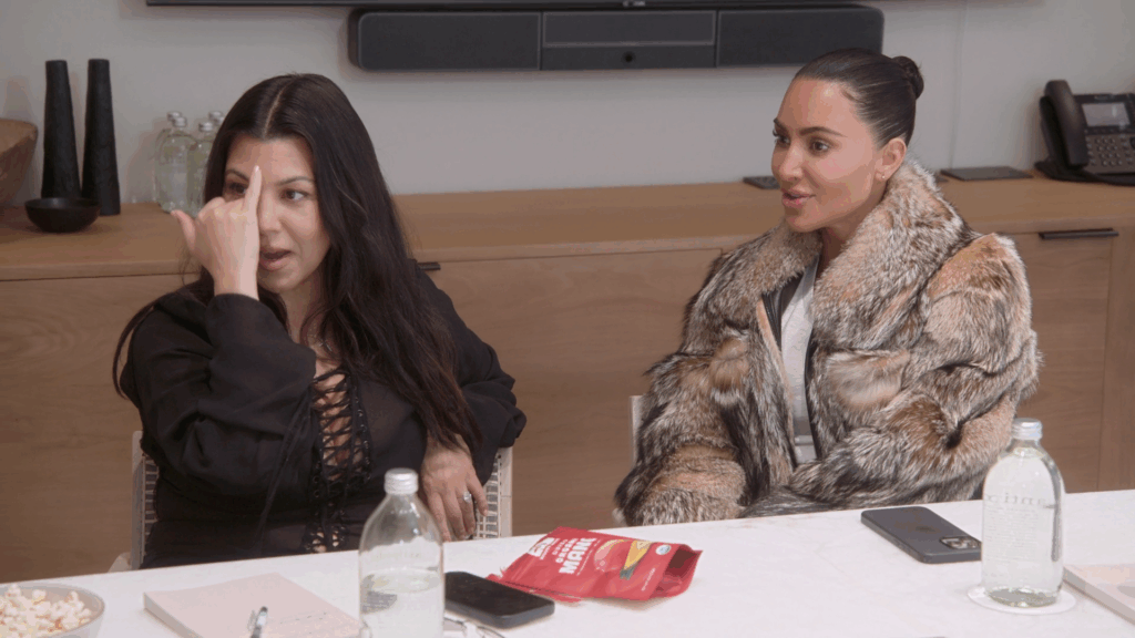 Kourtney Kardashian gestures beside Kim Kardashian.