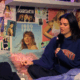Kendall Jenner sits on a bed in front of a collage of posters of sensible music tastes and films, all from Owen Thiele.