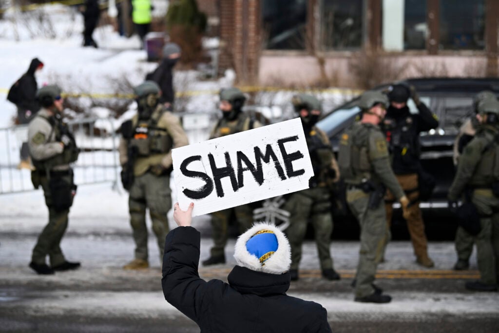 An onlooker holds a sign that reads "Shame" as members of law enforcement work the scene following a suspected shooting by an ICE agent during federal law enforcement operations on January 07, 2026 in Minneapolis, Minnesota. 