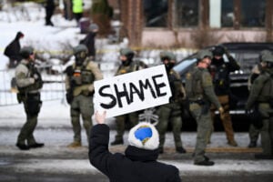 An onlooker holds a sign that reads "Shame" as members of law enforcement work the scene following a suspected shooting by an ICE agent during federal law enforcement operations on January 07, 2026 in Minneapolis, Minnesota.