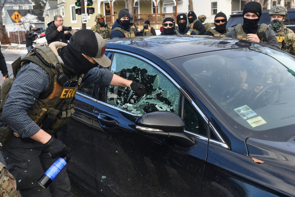 A federal officer breaks a car window as they begin the process of removing a woman from her vehicle near an area where ICE was operating in Minneapolis, Minnesota, on January 13, 2026.
