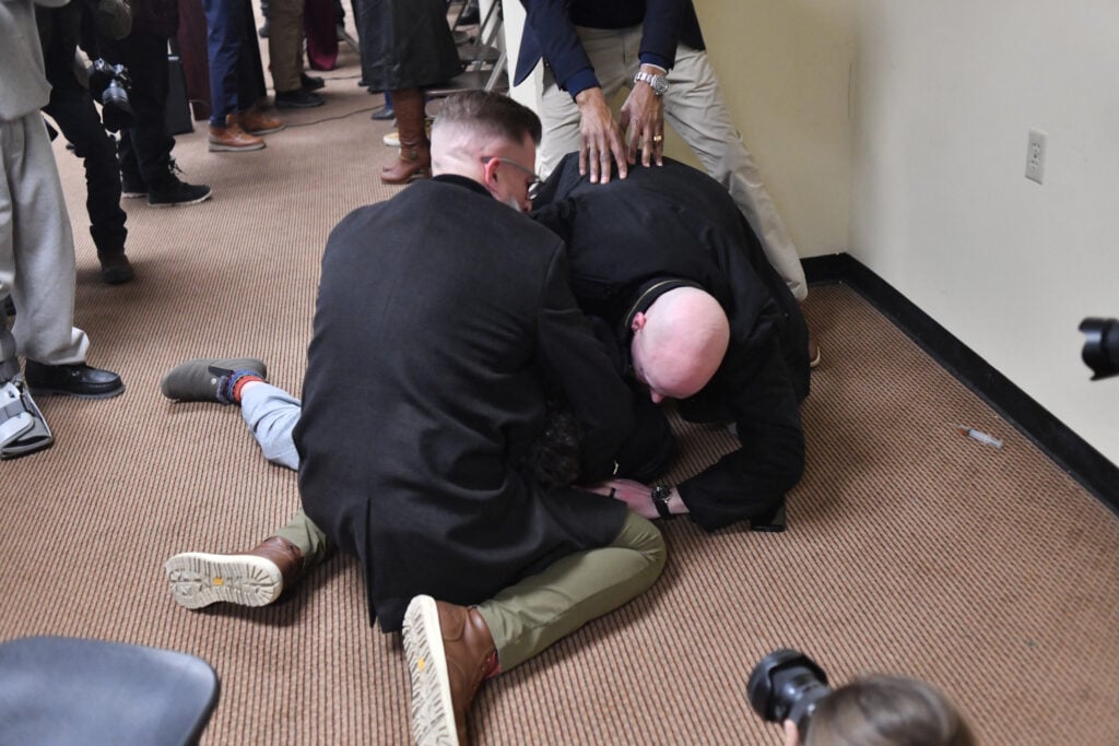 A man is tackled after spraying an unknown substance using a syringe (seen on the floor at R) at US Representative Ilhan Omar (D-MN) (out of frame) during a town hall she was hosting in Minneapolis, Minnesota, on January 27, 2026. 
