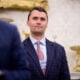 Turning Point USA co-founder Charlie Kirk stands in the back of the room as U.S. President Donald Trump speaks during a swearing in ceremony for interim U.S. Attorney for Washington, D.C. Jeanine Pirro in the Oval Office of the White House on May 28, 2025 in Washington, DC.