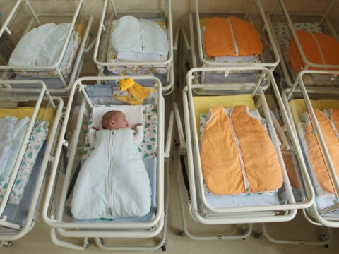 A 4-day-old newborn baby, who has been placed among empty baby beds by the photographer, lies in a baby bed in the maternity ward of a hospital.