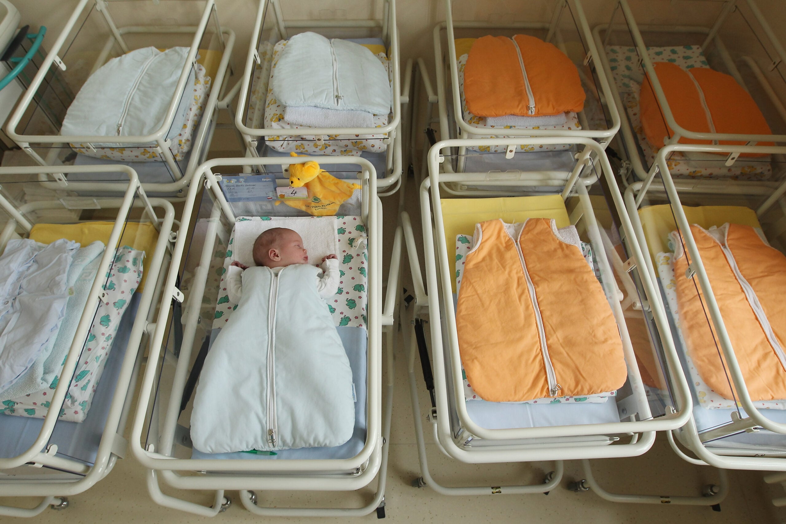 A 4-day-old newborn baby, who has been placed among empty baby beds by the photographer, lies in a baby bed in the maternity ward of a hospital.  