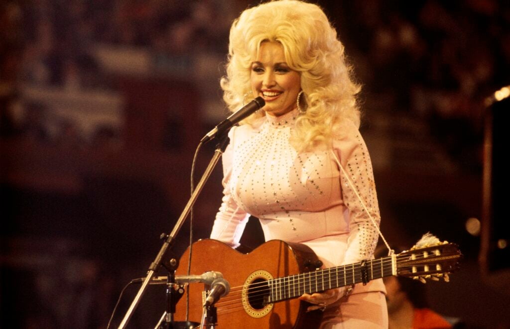 American singer, songwriter and actress Dolly Parton, performs with a guitar, 1976. 
