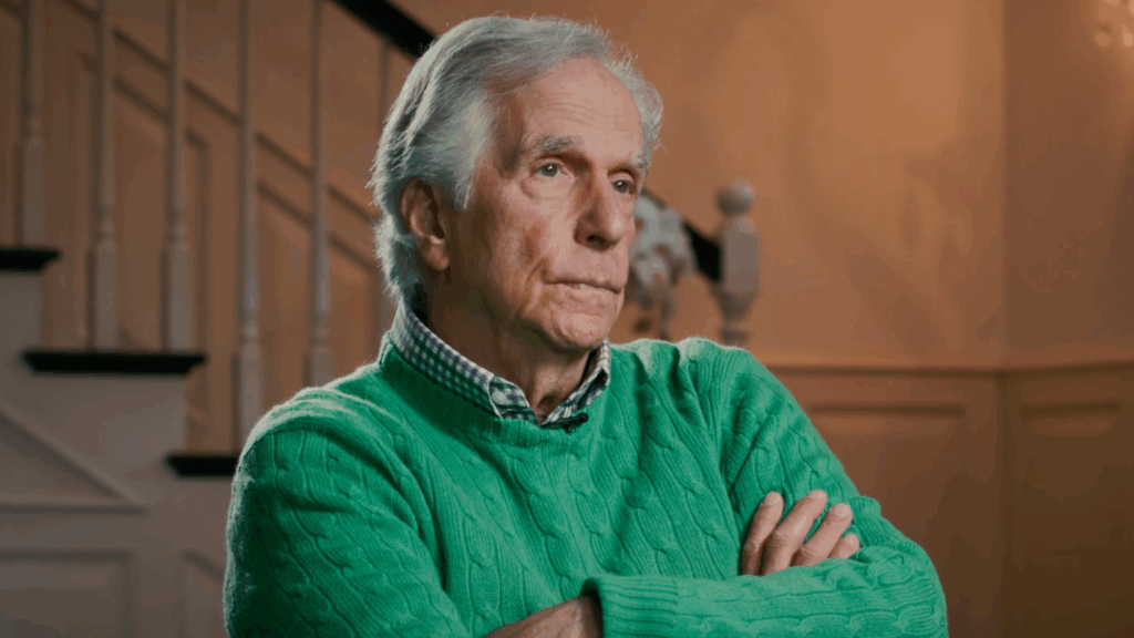 Henry Winkler in a lime green sweater but his arms crossed uncomfortably.