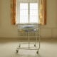 An empty baby bed, which has been placed under a window by the photographer.