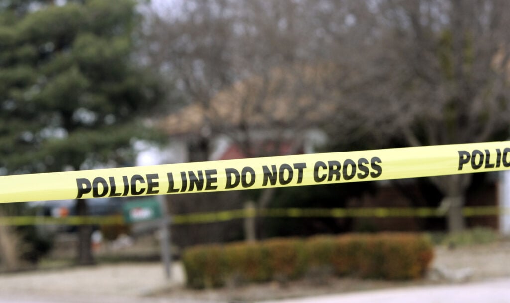 Police tape hangs across the street in front of a house.
