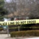 Police tape hangs across the street in front of a house.