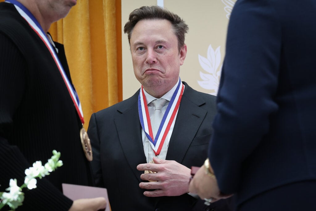 Elon Musk frowns while wearing an award in October 2026.